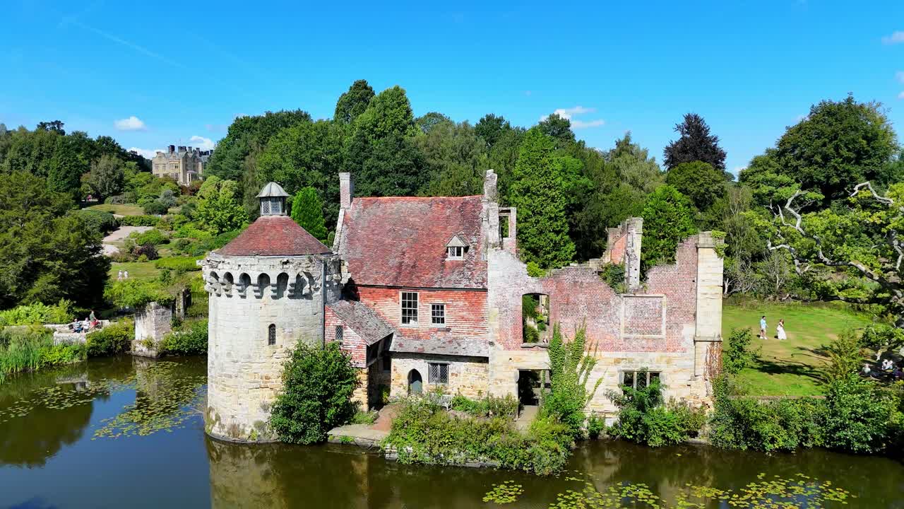 Luftfoto i filmisk stil af ruinerne af Scotney Castle i Kent. Middelalderlig stenarkitektur med voldgrav og haver, der giver et malerisk indblik i Storbritanniens landskab og historiske vartegn.