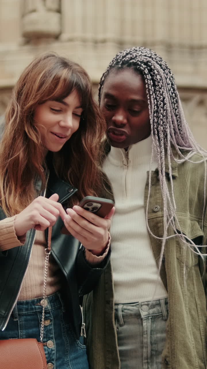 Happy Young Women Friends Sharing Content on Smartphone Outdoors