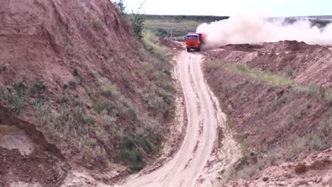 camión de descarga naranja conduciendo en un camino de tierra en una cantera, levantando polvo