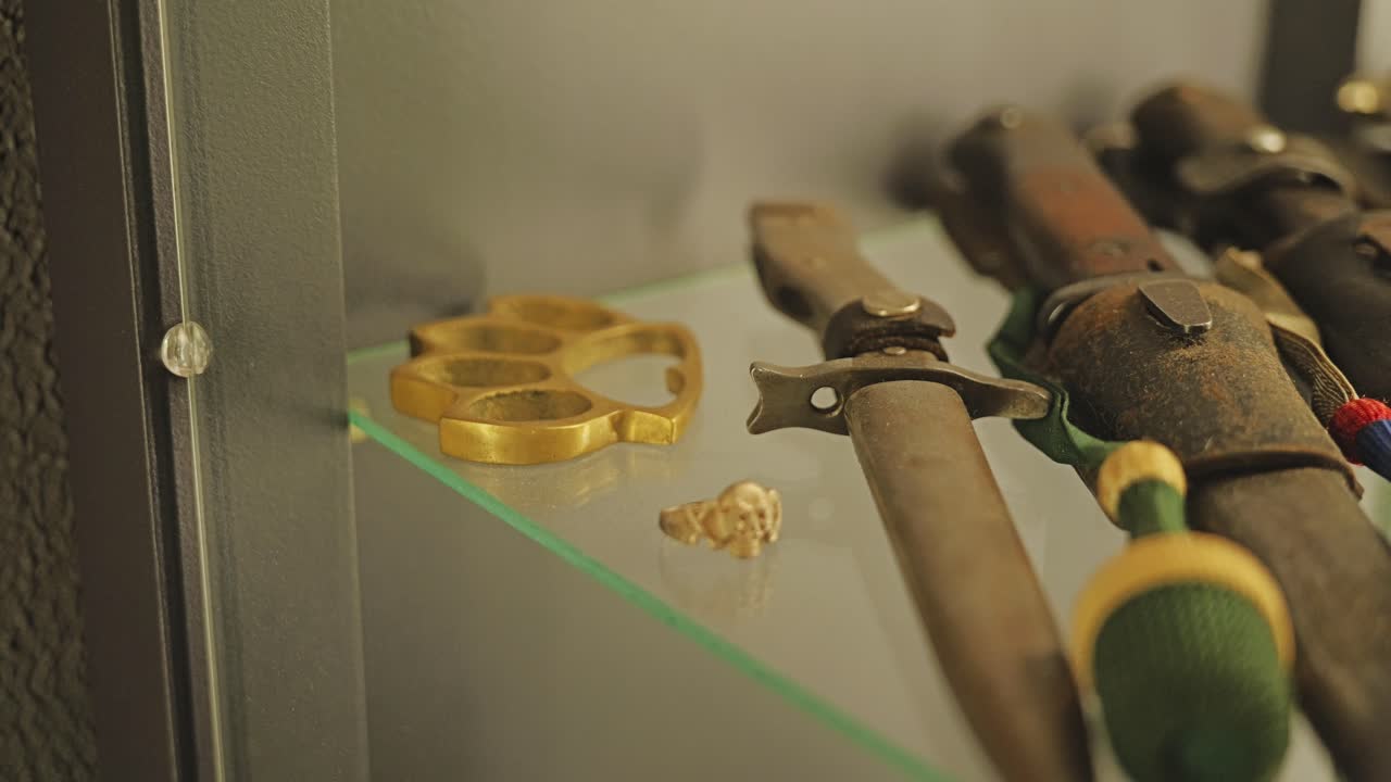 Close up of vintage brass knuckle and dagger with wood handle inside showcase