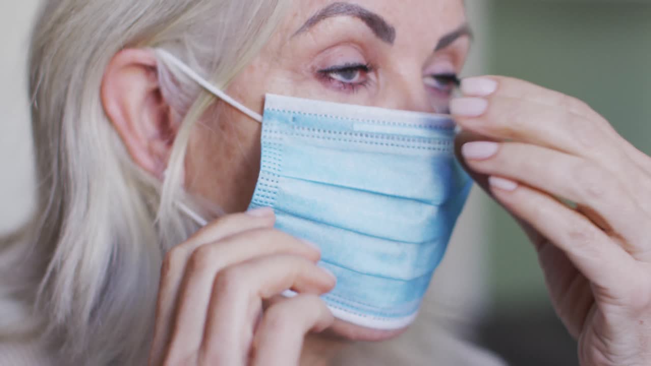 Retrato de mulher idosa caucasiana em casa ajustando a máscara facial.