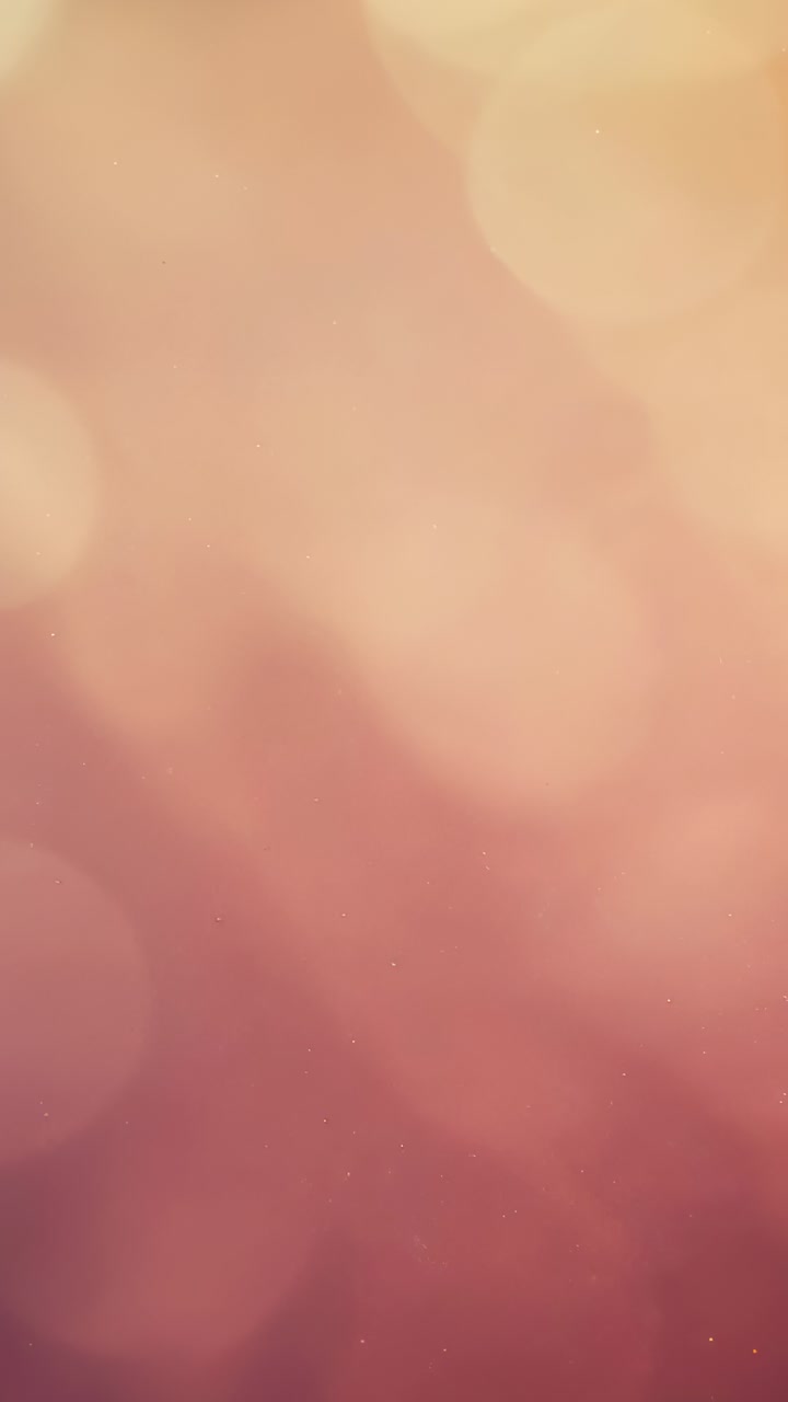 Vertical video: Advancing frames causing bokeh orbs drifting across closeup warm wash with grain