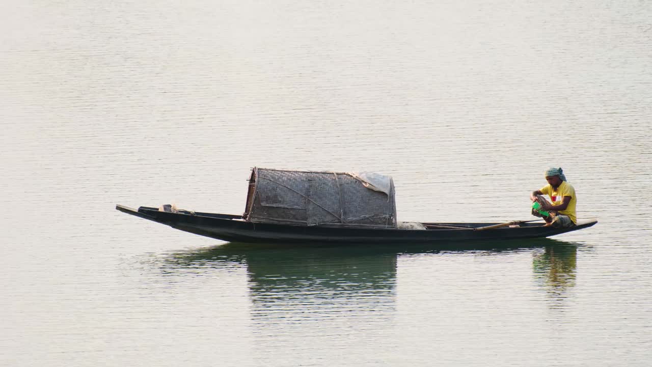 pescador sentado a bordo de un barco tradicional asiático, navegando por el río surma