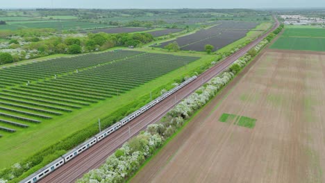 aerial drone view of solar power plant in england uk with trains passing photovoltaic panels on farmland