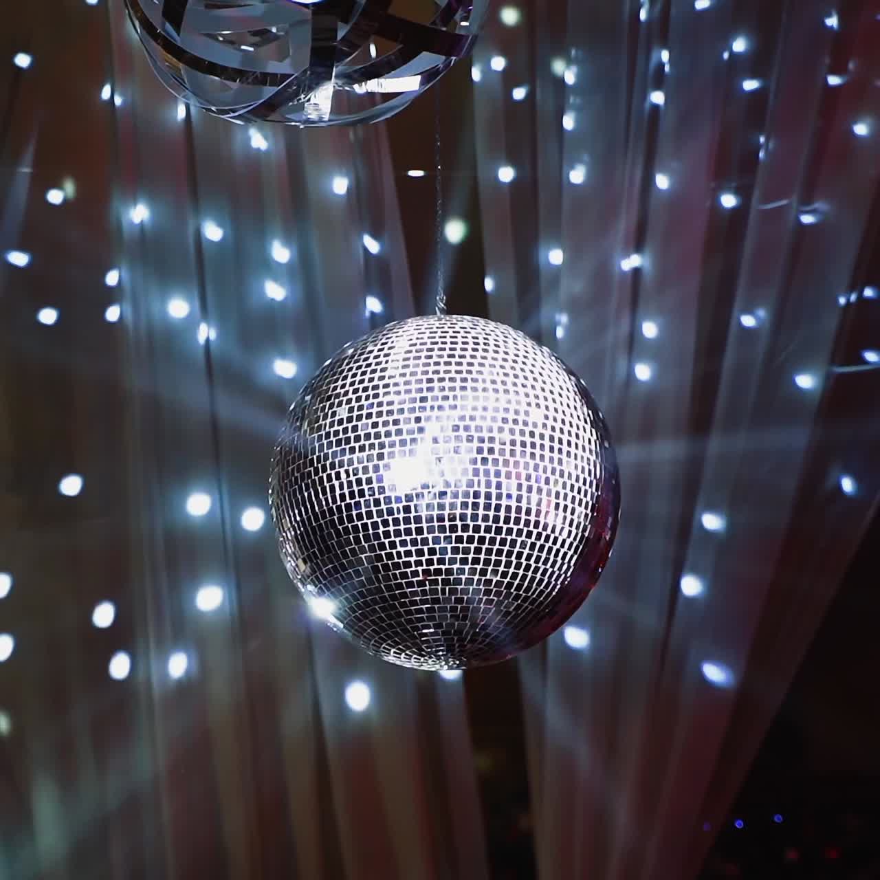 Silver shining disco ball. Mirror ball hanging from the ceiling and spinning against beautiful lights. Entertainment concept.