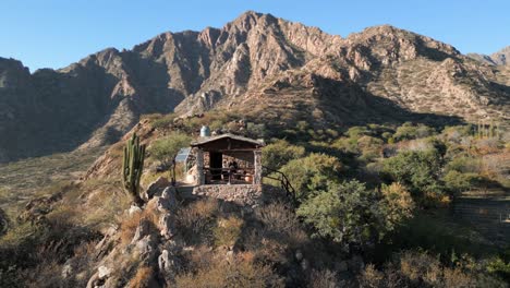 Aerial-circling-man-in-cabin-on-top-of-mountain-on-outskirts-of-Salta,-Argentina