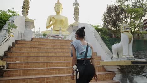 woman walking towards a golden buddha statue at a temple