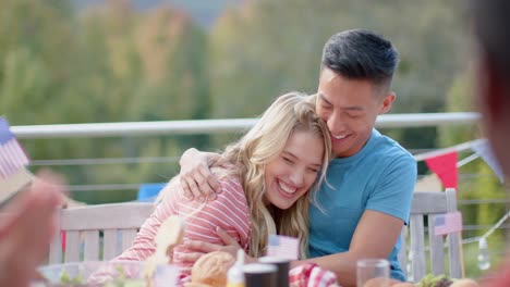 happy diverse friends embracing and smiling at dinner table in garden, slow motion