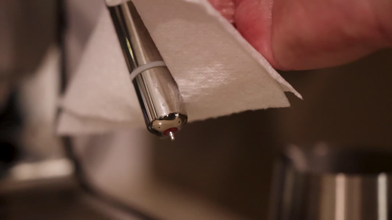 Close-up of hands cleaning a coffee machine steam wand with a cloth, highlighting hygiene and maintenance
