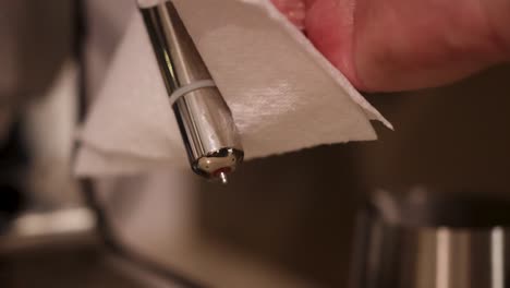 close-up of hands cleaning a coffee machine steam wand with a cloth, highlighting hygiene and maintenance
