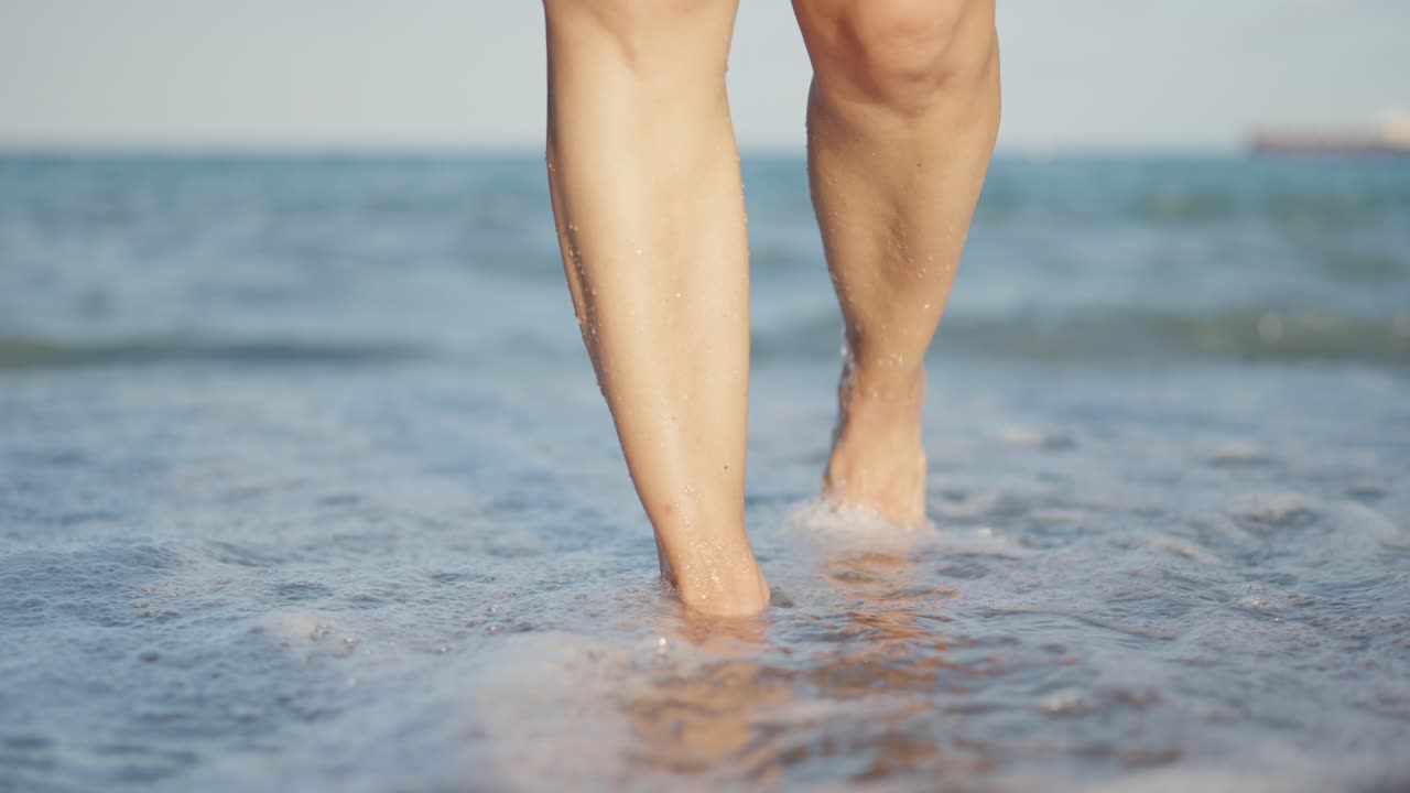 Close-up of bare legs and feet walking in ocean water at the beach