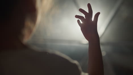 child plays with finger in room at backlight. little girl has fun with light and shadow in hotel closeup. curious kid palm against glowing lamp