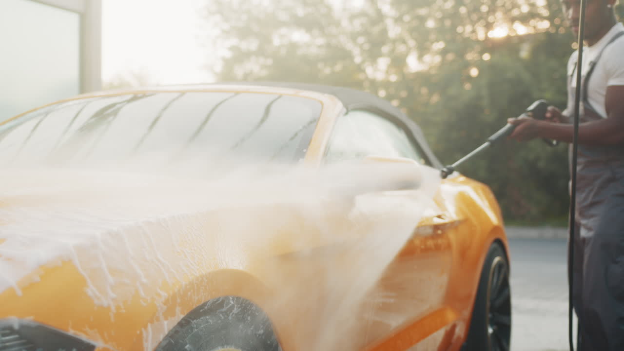 hombre lavando un coche convertible amarillo con una lavadora de alta presión