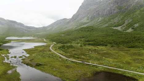 car driving on the narrow road by the lush mountain in hydalen, hemsedal on a foggy day - aerial panning shot