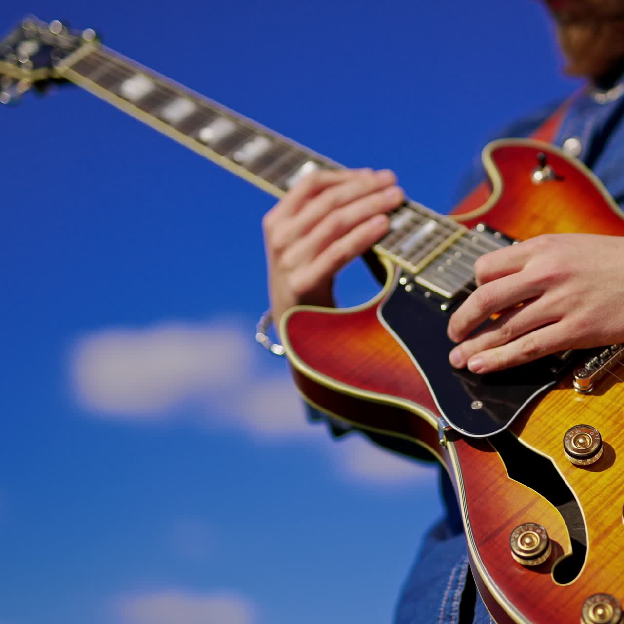 Kot pantolonlu beyaz bir adam yeşil tarlada şarkı söyleyerek gitar çalıyor. Arka planda davulcu bulanık bir şekilde davul çalıyor