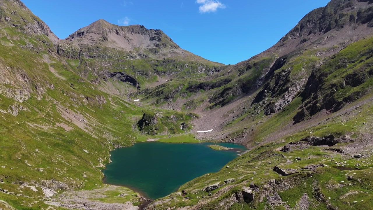 Et vidvinkelbillede af den turkise Lago Barbellino, der ligger i en frodig grøn dal i de italienske Alper under en klar blå himmel. Højalpint bjerglandskab til rejse- og naturdokumentarer.