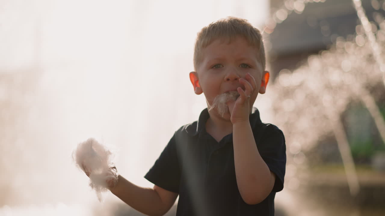 재미있는 유아 소년은 입에 큰 조각의 스핀 설탕을 넣습니다.