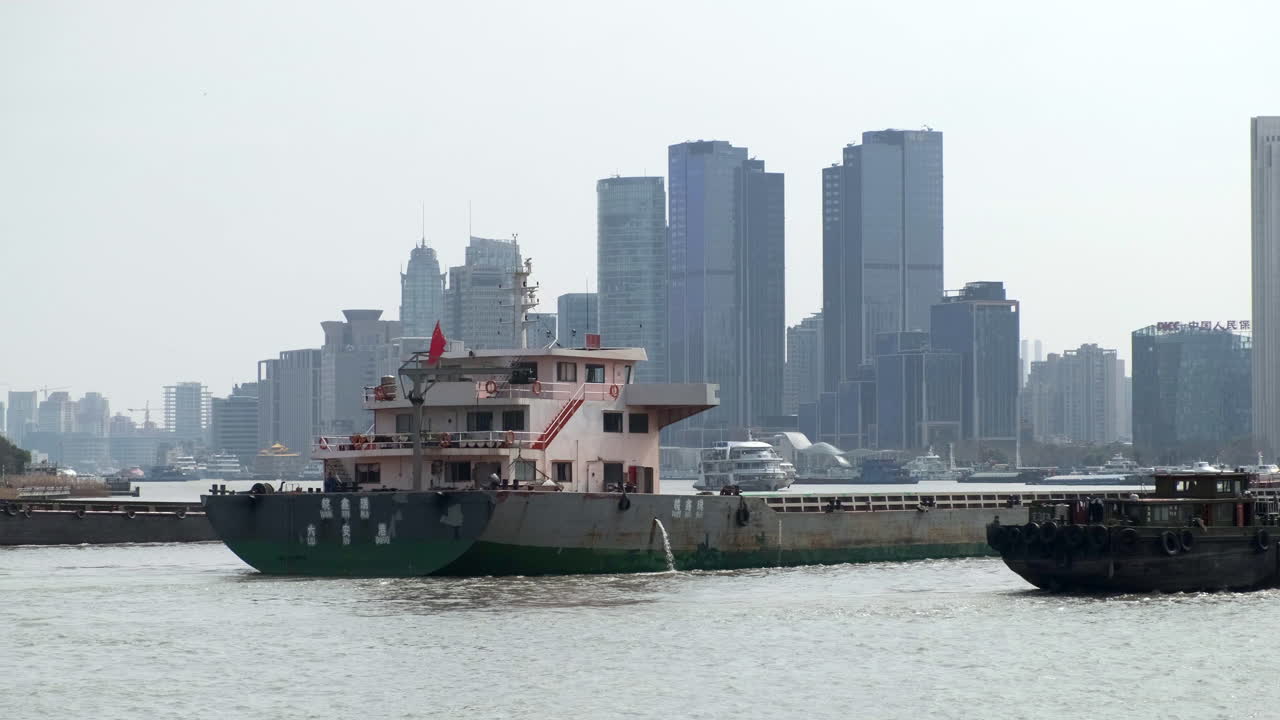 Cargo ship cruising along the Huangpu River with Shanghai’s modern skyline rising in the background on a hazy day