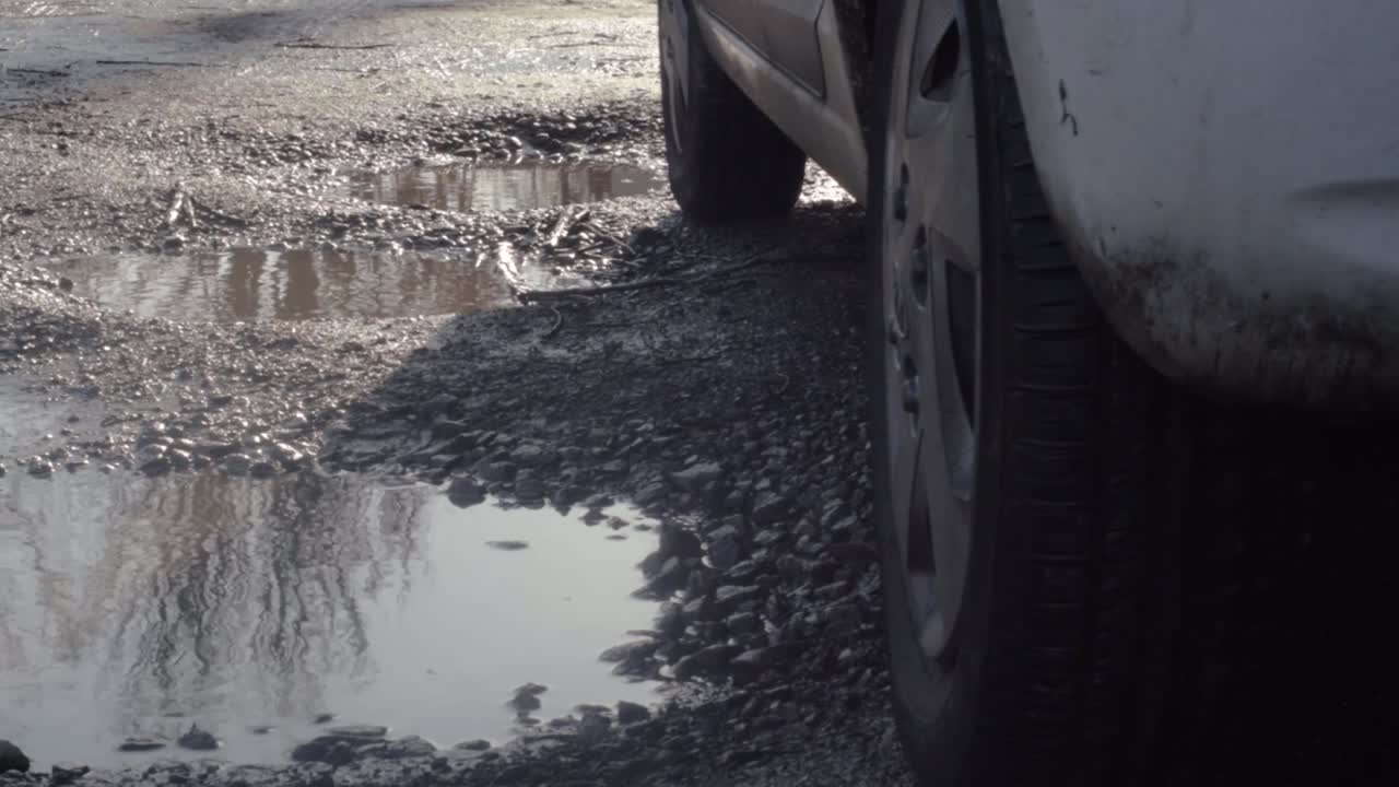 Car parked on road with muddy potholes