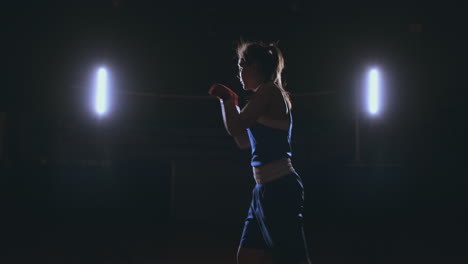 A-beautiful-sports-boxer-woman-in-red-bandages-on-her-hands-and-a-blue-t-shirt-is-fighting-with-a-shadow-practicing-the-speed-and-technique-of-punches.-Camera-movement-side-View.-Steadicam-shot.-Preparing-for-self-defense