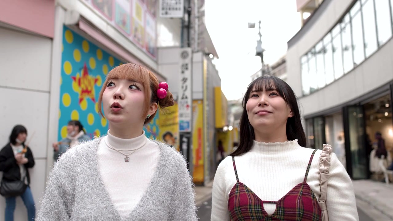 手持ちのミディアムショットで、2人の友人が賑やかな商店街を探索し、店のショーウィンドウを指差している。