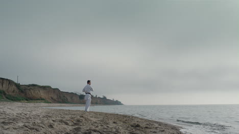 sportsman training karate exercises on beach. athlete practicing martial arts.