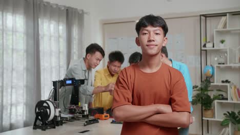 grupo de jóvenes niños asiáticos con impresión 3d y una computadora portátil trabajando en casa, un niño sonriendo y cruzando los brazos a la cámara mientras sus amigos discuten sobre una mano cyborg