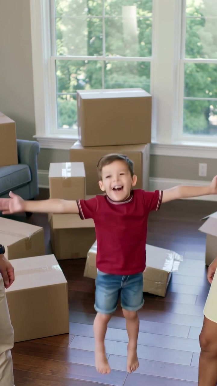 Vertical video: Jumping barefoot boy in red tee reacting to parents high-five at home with boxes