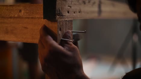 Closeup of a male carpenter using a hammer to hammer the nails in a wooden plank, carpenter building furniture for home in his workshop