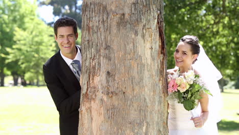 happy newlyweds posing in the park beside a tree