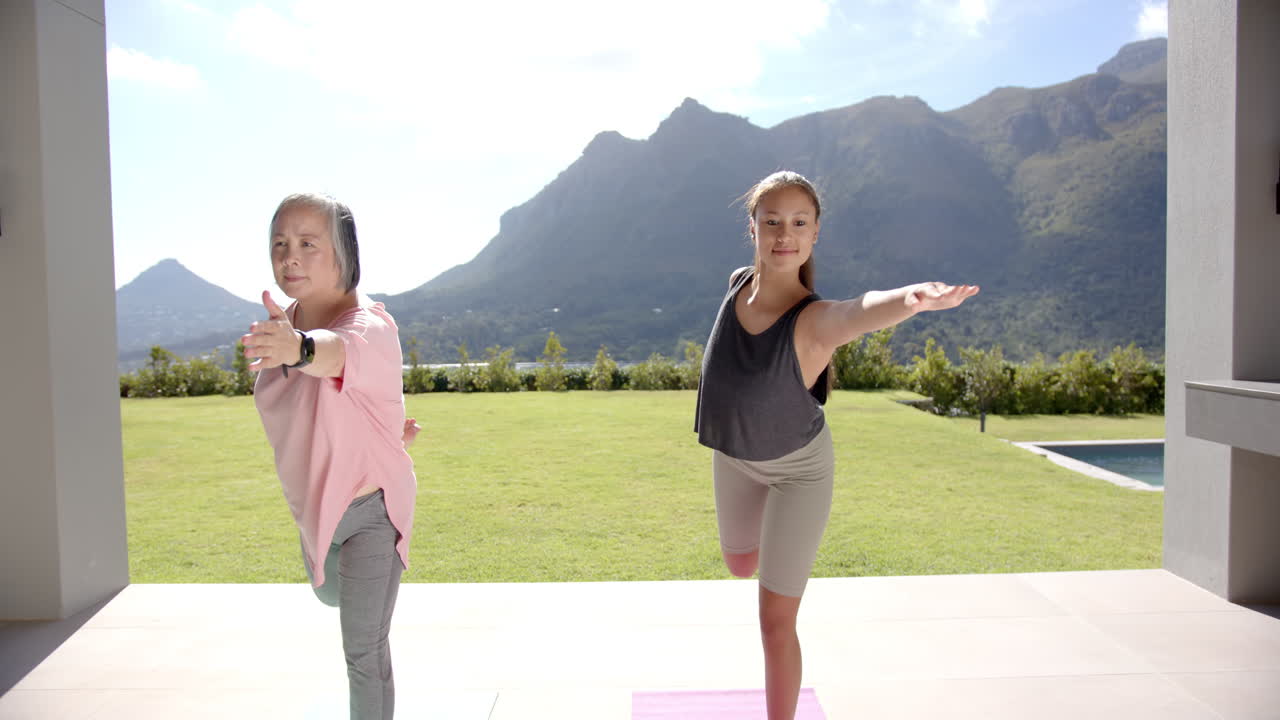 Practicing yoga, asian grandmother and granddaughter balancing on one leg outdoors