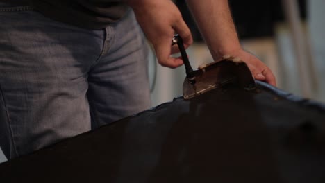 young man unscrewing a screw from a couch with rusted supports under tungsten light