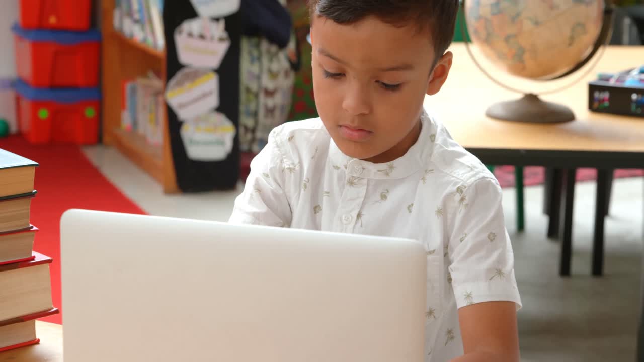 vista frontal de un escolar asiático atento estudiando con una computadora portátil en un aula de la escuela 4k