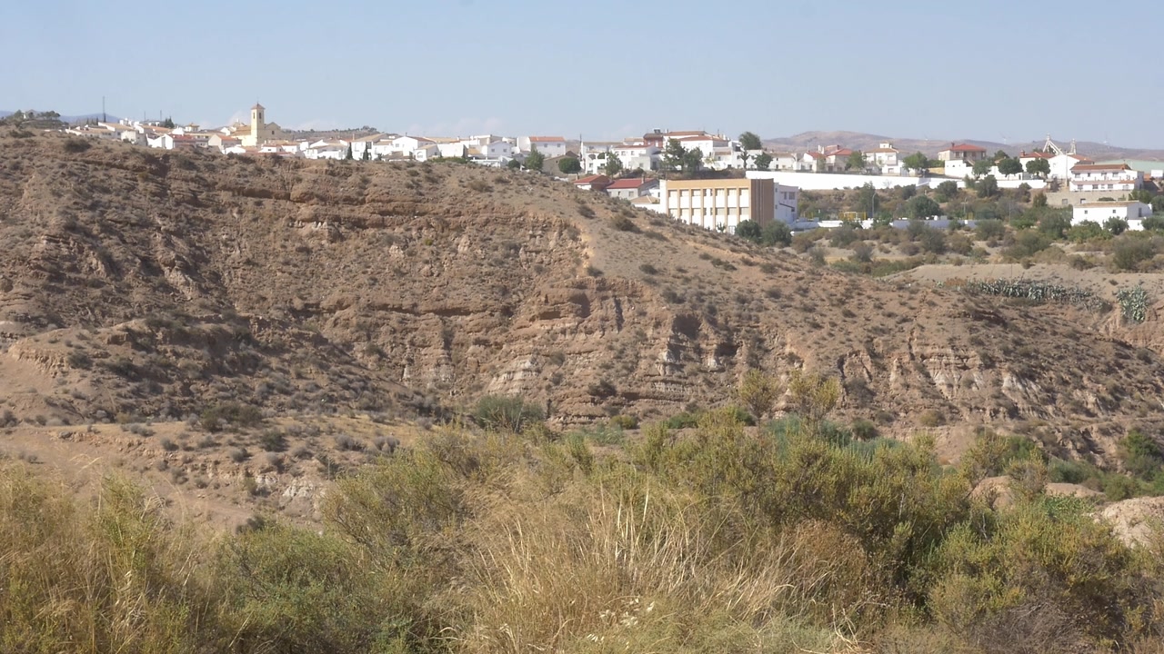 Wide shot of the traditional white village of Taberno and San Jose Church in Almeria. View from a dry canyon with green bushes in the foreground. Authentic rural Andalusian landscape and blue sky.