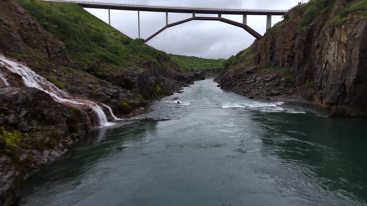 Aerial view of the Jökulsá River bridge in Iceland, showing flowing water, surrounding rugged terrain, and wide open landscape under clear sky