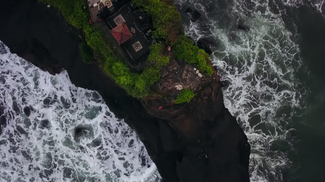 Cliffside temple on a rocky island, waves crashing below, aerial view of Tanah Lot