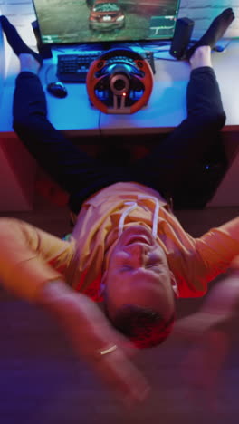 top view of man driving simulator. young man with pc computer playing car racing video game at home. vertical video