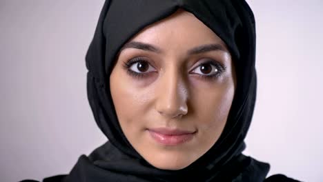 young muslim girl in hijab opens eyes and watches at camera, dreaming concept, grey background