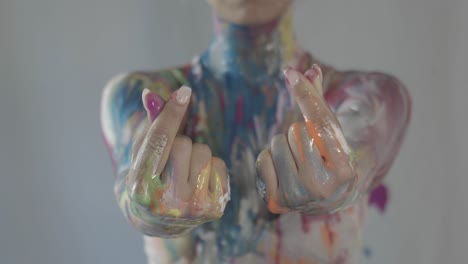 close up of a woman's hands making finger hearts, covered in fresh colorful paint all over her body