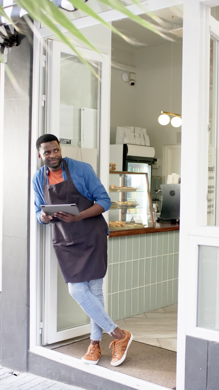 Vertical video: Standing at cafe entrance, male barista holding tablet and smiling confidently