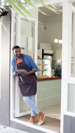 vertical video: standing at cafe entrance, male barista holding tablet and smiling confidently
