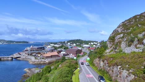 a black car travels on a scenic coastal road beside loch alsh, passing rocky hills and a small port town under bright daylight with clear skies