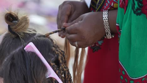 traditional african woman doing braids to a tourist girl in her hair