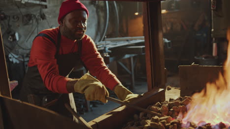 black man heating metal billet in forge fire at work in smithy