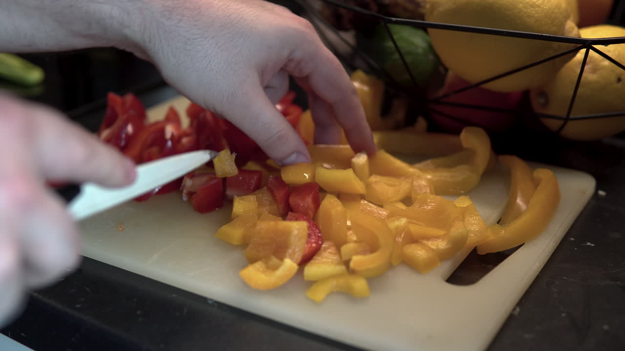 Yellow peppers slicing on the plastic board, colour fruits in background