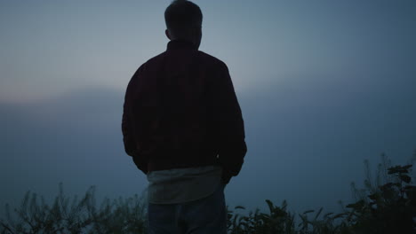 relaxed man enjoying sunrise in field. calm guy looking mountain landscape