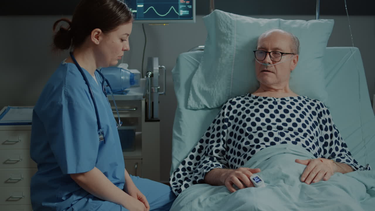 Nurse from hospital ward tends to sick old patient in bed