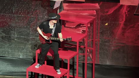 man in cowboy hat plays red electric guitar on stage, copy space