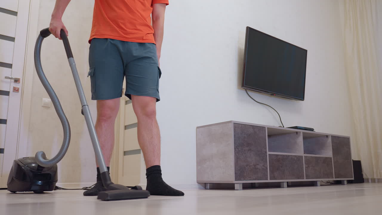 Close up of man vacuuming light wooden floor with modern cleaner, black socks visible while standing on clean surface, concept of household chores, hygiene maintenance