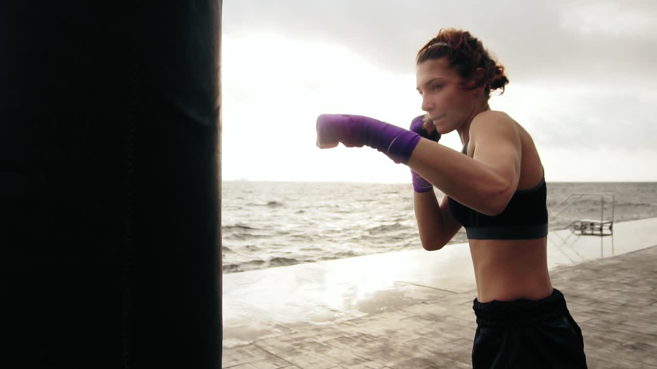 vista de cerca de una mujer joven entrenando con la bolsa de boxeo contra el hijo. sus manos están envueltas en cintas de boxeo púrpura